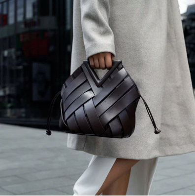 Person holding a brown veya handbag with a blurred urban background